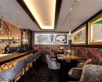 Ein modernes Restaurant mit stilvoller Einrichtung und einer langen Bar. Die Wände sind mit bunten Mustern und Kunstwerken dekoriert.