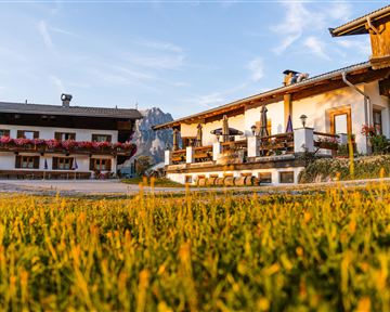 A charming farmhouse with beautiful flower planting is situated in a picturesque landscape. The gentle morning light creates an inviting atmosphere.