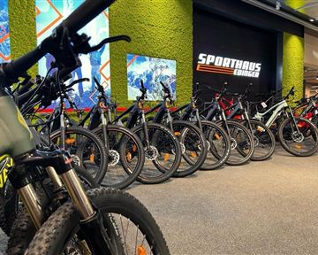 Eine Auswahl von Mountainbikes in einem Sportgeschäft. Im Hintergrund ist das Logo von "Sporthaus Edinger" zu sehen.