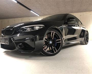 Ein sportlicher BMW in einem modernen Parkhaus. Das Auto ist schwarz mit auffälligen Felgen und einem dynamischen Design.