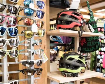 Eine Auswahl an Sonnenbrillen und Fahrradhelmen steht in einem Geschäft aus. Im Hintergrund sind verschiedene Accessoires sichtbar.