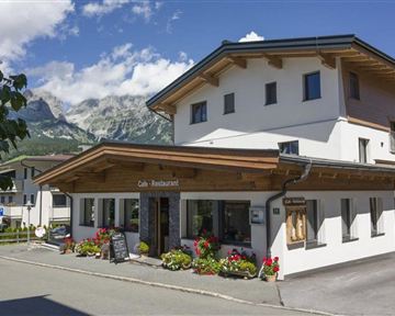 Ein gemütliches Restaurant mit einer schönen Holzveranda. Im Hintergrund sind die Berge und ein klarer blauer Himmel zu sehen.