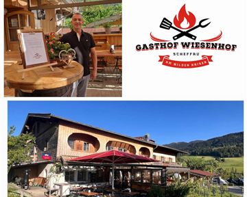 Ein einladender Gasthof mit einem gemütlichen Restaurantbereich und schöner Außenterrasse. Im Hintergrund ist der Gasthof Wiesenhof zu sehen, umgeben von grüner Landschaft.