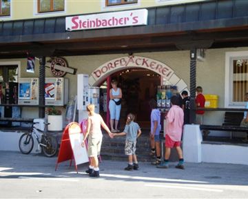 Eine traditionelle Dorfbäckerei mit einem Eingang, der Gäste anzieht. Kinder stehen in der Nähe und warten auf ihre Leckereien.
