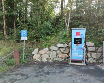 A charging station for electric cars in a forested area. Next to the station is a parking sign.