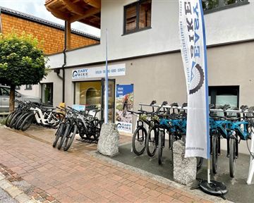 Ein Geschäft mit mehreren E-Bikes, die auf dem Gehweg ausgestellt sind. Über dem Geschäft weht ein Fahne mit dem Schriftzug "EASY BIKE".