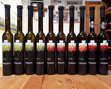 A series of bottles with olive oil stands on a wooden tray. The bottles have different labels in various colors.