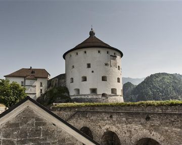 Eine historische Festung mit einem runden Turm und einem beeindruckenden Ausblick auf die umliegenden Berge. Die Architektur ist auffällig und spiegelt vergangene Zeiten wider.
