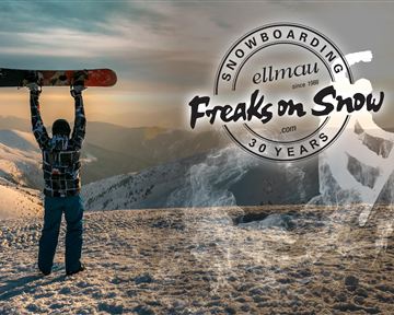 Ein Snowboarder steht auf einem Berggipfel und hält sein Snowboard hoch. Im Hintergrund sind verschneite Berge und ein sonniger Himmel zu sehen.