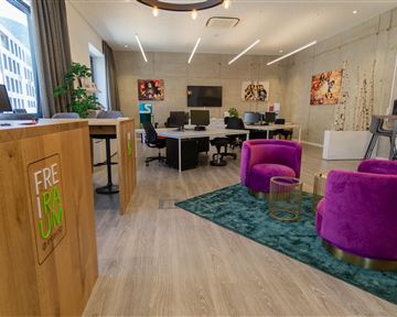 Ein modernes Büro mit hellen Farben und stilvollen Möbeln. Im Vordergrund sind zwei lila Sessel auf einem Teppich zu sehen.