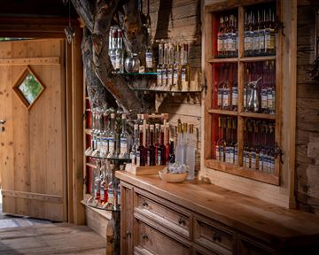 A cozy wooden room with a wooden dresser and shelves full of jars. The door in the background has a green window and invites you outside.