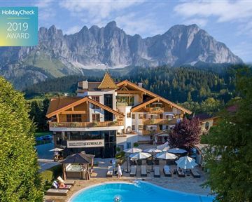 A beautiful hotel with a pool and loungers, surrounded by picturesque mountains. The nature in the background creates a relaxed atmosphere.