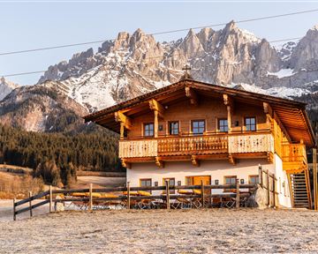 A traditional wooden house in the mountains, surrounded by snow-capped peaks. The landscape is peaceful and idyllic.