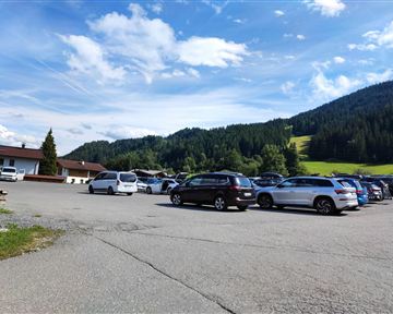 Ein Parkplatz mit mehreren Autos und einer schönen Berglandschaft im Hintergrund. Der Himmel ist klar mit einigen Wolken.