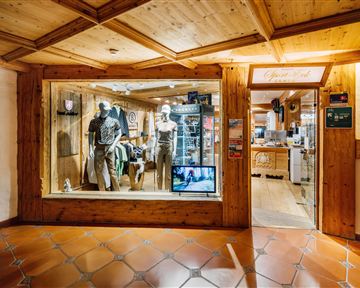 A store with wooden siding and a showcase displaying clothing on mannequins. In the background, additional products and a reception desk can be seen.