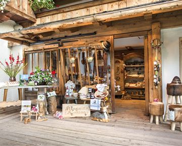 Ein rustikaler Laden mit Holzverzierungen und einer einladenden Schaufensterdekoration. Vor der Tür stehen Pflanzen und handgefertigte Artikel zum Verkauf.