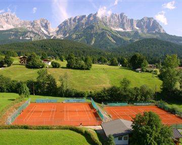 Two tennis courts in the midst of a picturesque mountain landscape. Green meadows and high mountains create the perfect backdrop.