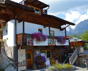 Ein charmantes Holzhaus mit einem Balkon voller Blumen. Im Hintergrund sind Berge und ein klarer Himmel zu sehen.