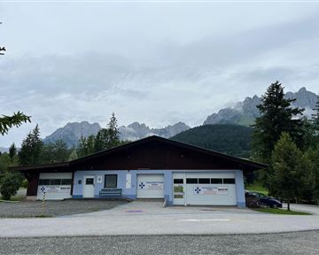 A modern building in a natural environment, surrounded by trees and mountains. The sky is cloudy and there is a calm atmosphere.
