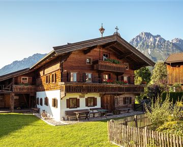 Ein traditionelles Holzhaus in den Alpen mit einem gepflegten Garten. Im Hintergrund sind majestätische Berge zu sehen.