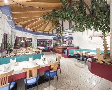 Ein gemütliches Restaurant mit Holzdecke und farbigen Sitzplätzen. Die Tische sind festlich gedeckt und bieten Platz für viele Gäste.