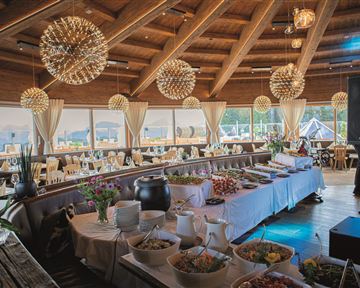 Ein elegantes Restaurant mit Holzdach und großen Fenstern. Auf dem Tisch steht eine Vielzahl von Speisen und Dekorationen.