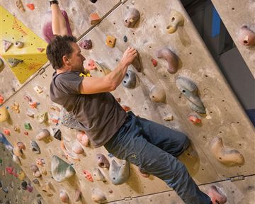 A climber navigating a climbing wall with various grips. The wall is colorful and has numerous small holds.