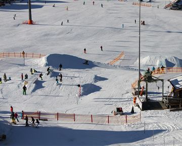 A lively winter sports landscape with many people skiing and snowboarding. The snow is fresh and the atmosphere is cheerful.
