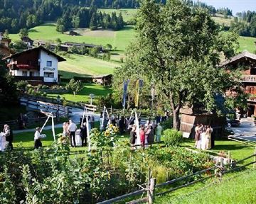 A festive outdoor event with guests in a green garden. Traditional farmhouses and gentle hills can be seen in the background.