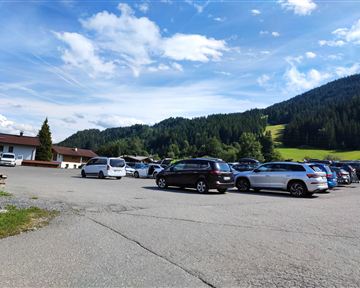 Ein Parkplatz mit mehreren Autos und einer schönen Berglandschaft im Hintergrund. Der Himmel ist klar mit einigen Wolken.