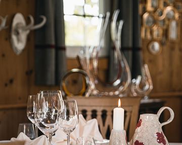A stylishly set table with glasses, napkins, and a candle. In the background, wooden paneling and decorative elements are visible.