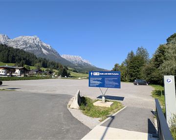 Ein Parkplatz in den Bergen mit klarer Sicht auf die umliegenden Gipfel. Der Himmel ist blau und die Umgebung ist grün und einladend.