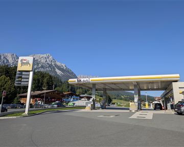 Eine Tankstelle vor einer malerischen Berglandschaft. Der Himmel ist klar und blau.
