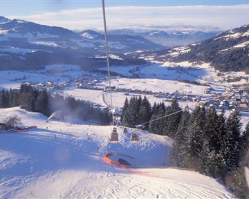 Eine wunderschöne Winterlandschaft mit verschneiten Bergen und einem Skilift. Im Hintergrund ist ein ruhiges Dorf zu sehen.