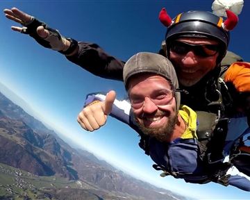 Ein mutiger Tandemsprung mit einem scherzenden Fallschirmspringer. Im Hintergrund sind die beeindruckenden Berglandschaften zu sehen.