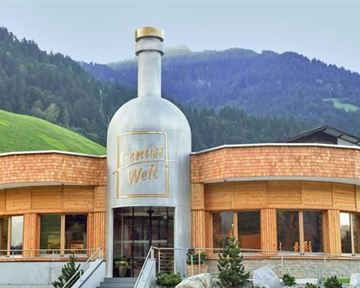 Ein modernes Gebäude in Form einer Flasche befindet sich in einer malerischen Berglandschaft. Grüne Wiesen und Hügel umgeben die Architektur.