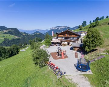 A picturesque mountain cabin surrounded by green meadows and mountains. The outdoor area offers play options and a relaxed atmosphere.