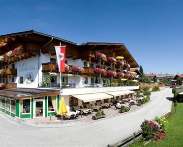 Ein gemütliches Hotel im alpinen Stil mit Balkonen, die mit Blumenkästen geschmückt sind. Umgeben von einer malerischen Landschaft und viel Grün.