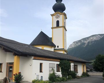 A colorful church with a tall tower and a distinctive dome. In the background, impressive mountains can be seen.