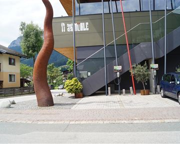 A modern designed building with an attractive sculpture in the foreground. Electric charging stations are visible on the sidewalk.