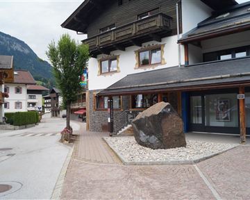 Eine ruhige Straße mit traditionellen Gebäuden und einem großen Stein in der Mitte. Im Hintergrund sind grüne Berge zu sehen.