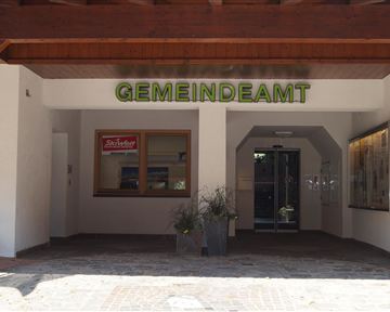 An entrance area of the municipal office with a clear sign. Next to the door, there is a windowsill with a plant.