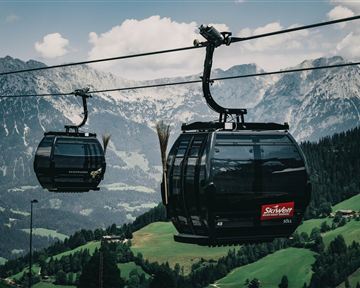 A cable car travels through a picturesque mountain landscape. In the background, high mountains and green meadows can be seen.