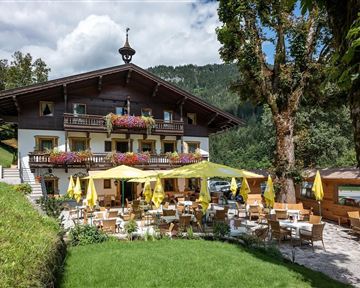 A cozy restaurant in the mountains with an inviting terrace. Yellow sun umbrellas and flowers adorn the outdoor areas.