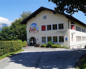 A beautiful building in a rural setting with a painting on the wall. There are trees and a quiet road leading to the building.