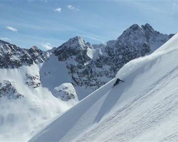 Eine wunderschöne winterliche Berglandschaft mit schneebedeckten Gipfeln. Ein Skifahrer fährt die Piste hinunter und hinterlässt eine Spur im frischen Schnee.