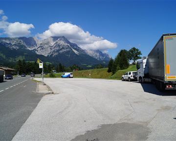 A clear view of majestic mountains under a blue sky. Some vehicles are parked by the roadside in a tranquil setting.