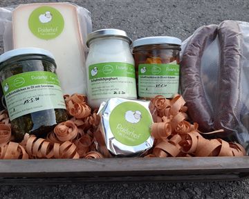 A basket with various foods, including cheese, yogurt, and pickled vegetables. Everything is nicely arranged in a bed of paper strips.