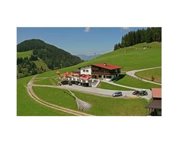 A picturesque mountain cabin with a red roof amidst green meadows. The surroundings are hilly and wooded, ideal for a relaxing stay in nature.