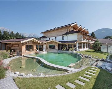 Ein modernes Haus mit hellem Holz und großen Fenstern. Der Garten hat einen Pool und ist von grünen Wiesen und Bäumen umgeben.